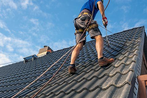 Håndværker maler tagsten, iført sikkerhedssele på tag med blå himmel