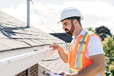 Professionel håndværker udfører tagtjek og inspicerer tagrender på hus.